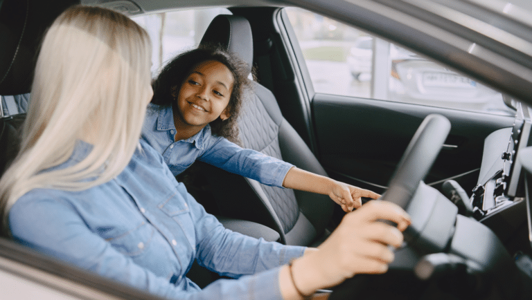 An inquisitive child trying out all the new gadgets in a modern car with her mom.